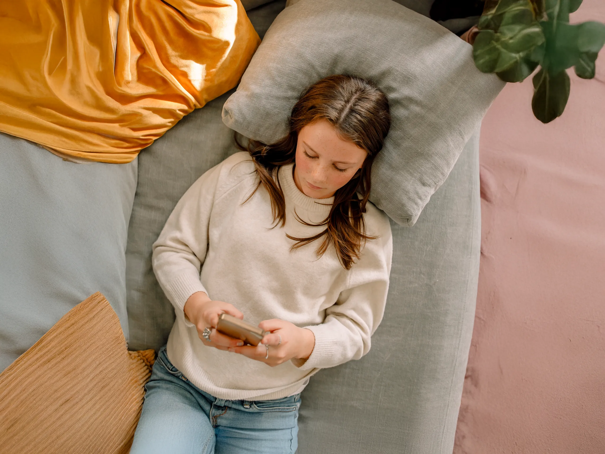 Girl lying on a bed looking at a smartphone.