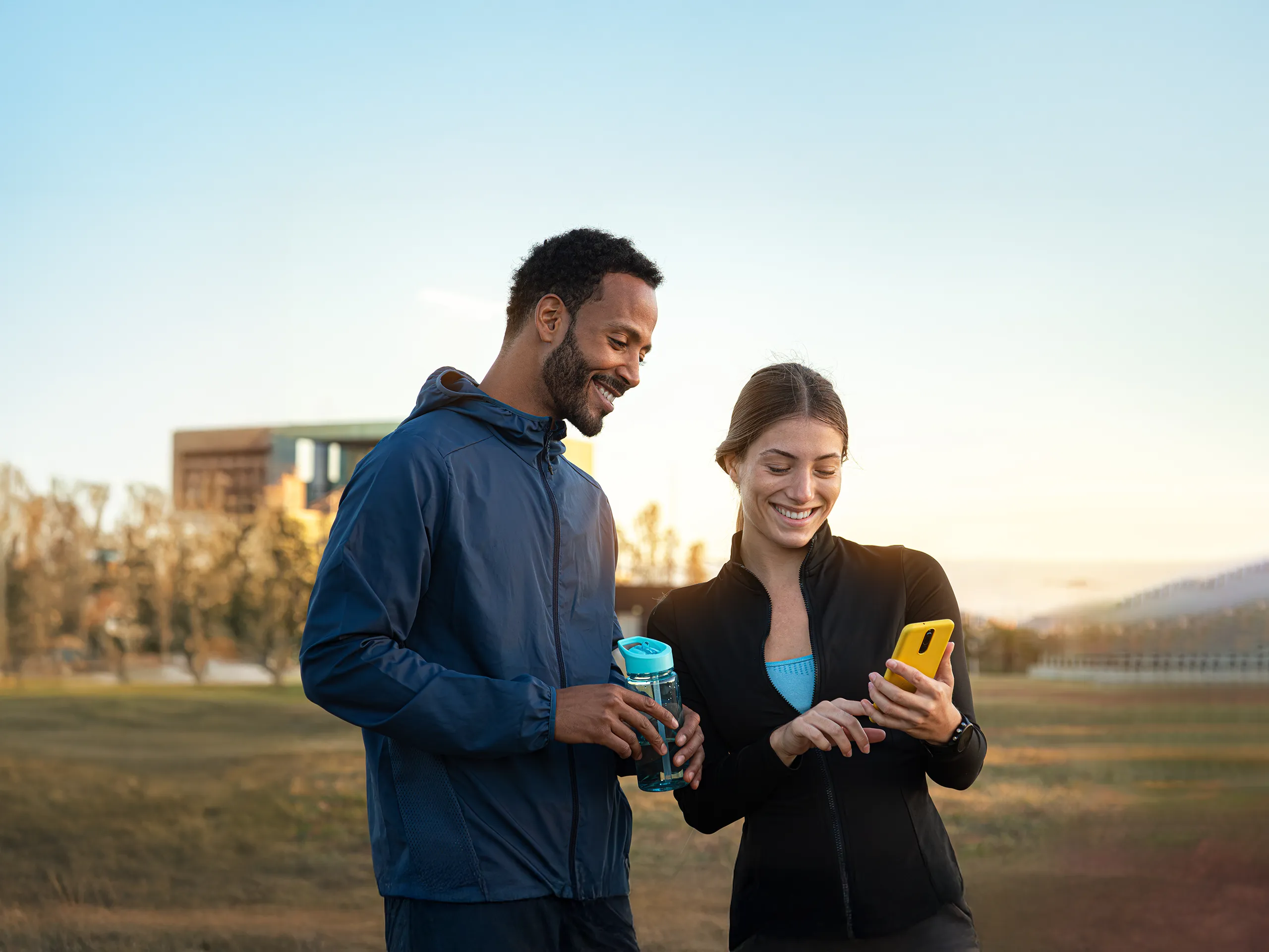 Two people laughing while looking at a smartphone after jogging.