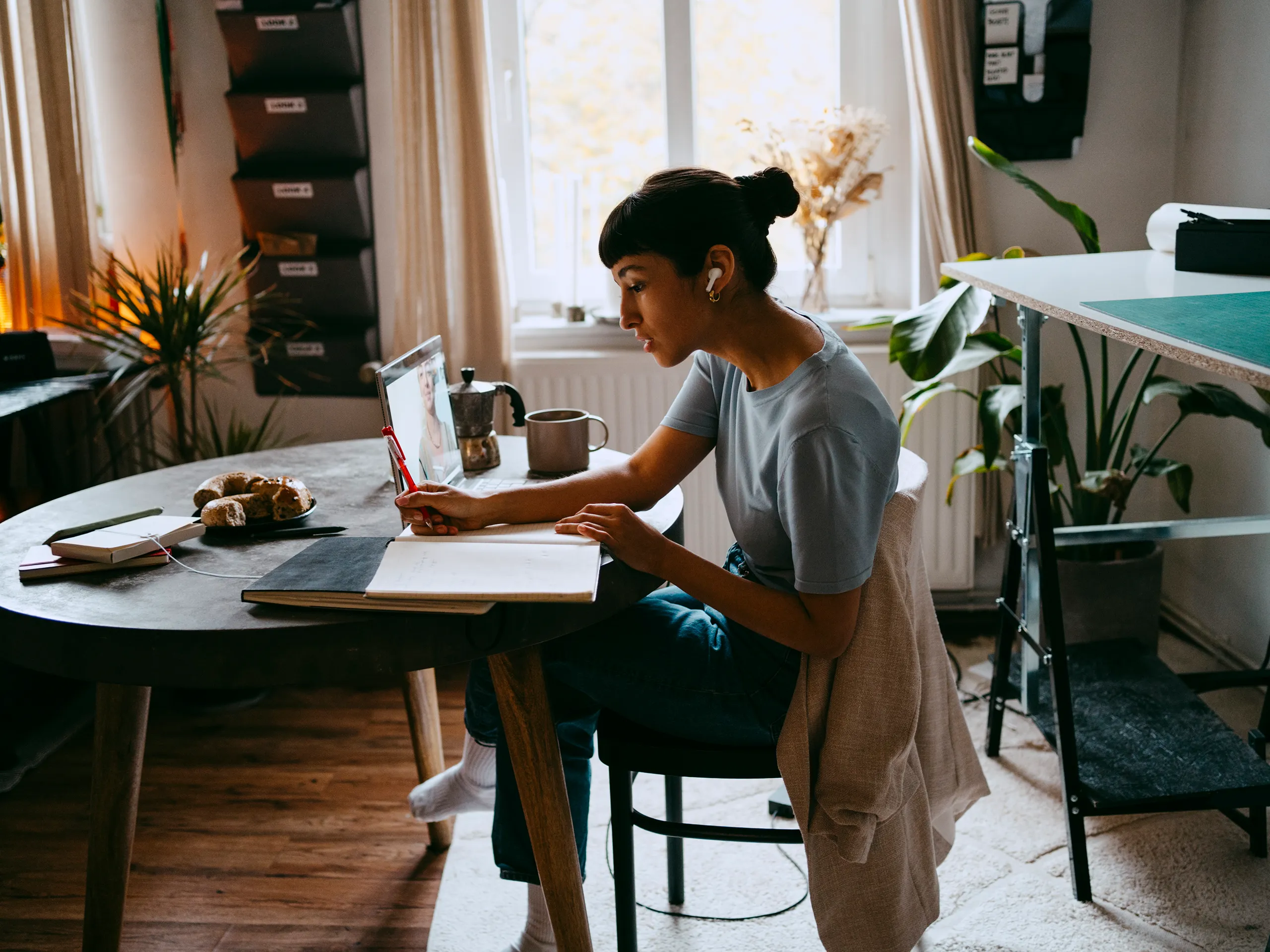 Woman working from home, writing notes while on a video call.