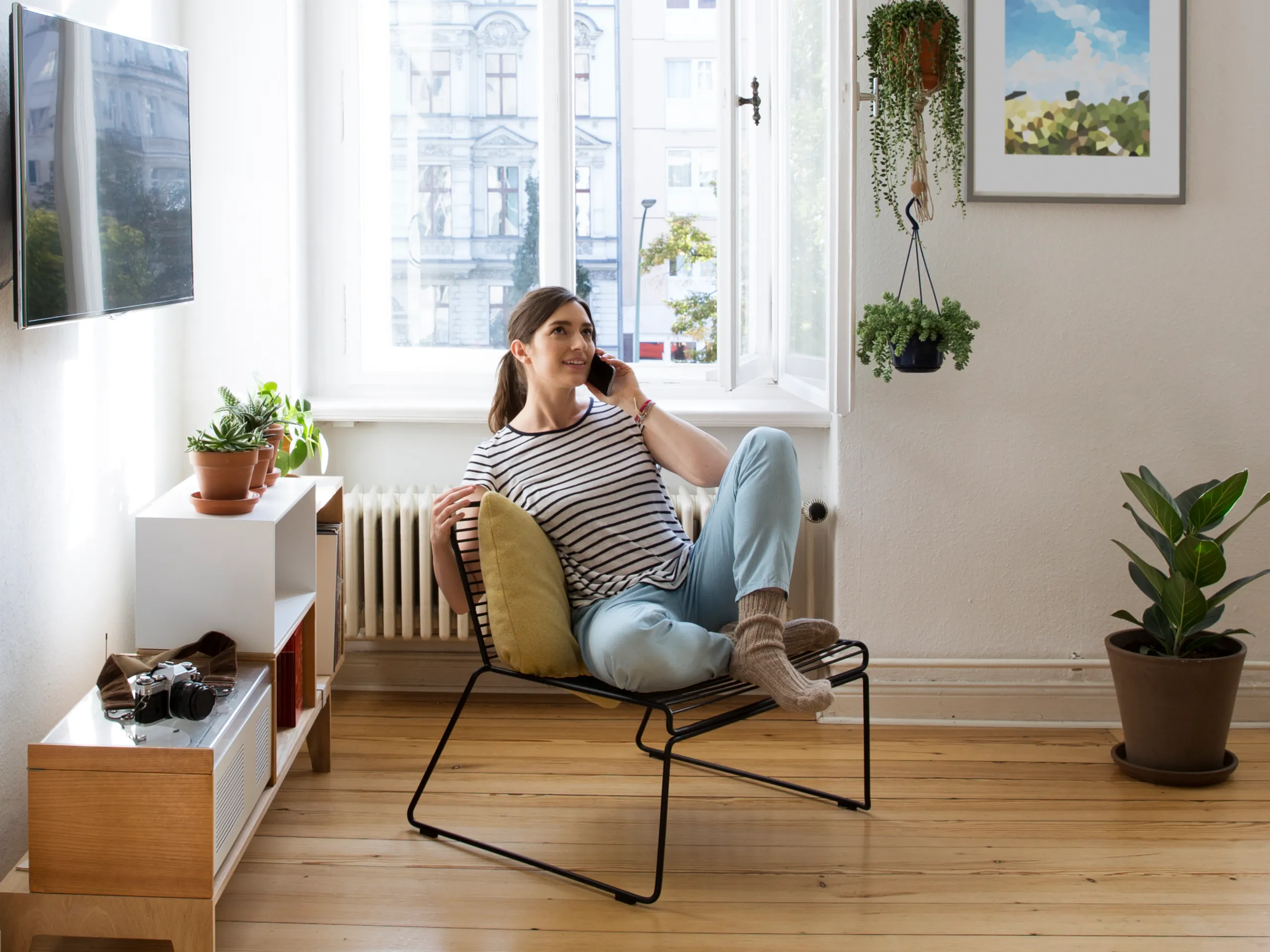 Woman sits relaxed in a modern living room and talks on the phone.