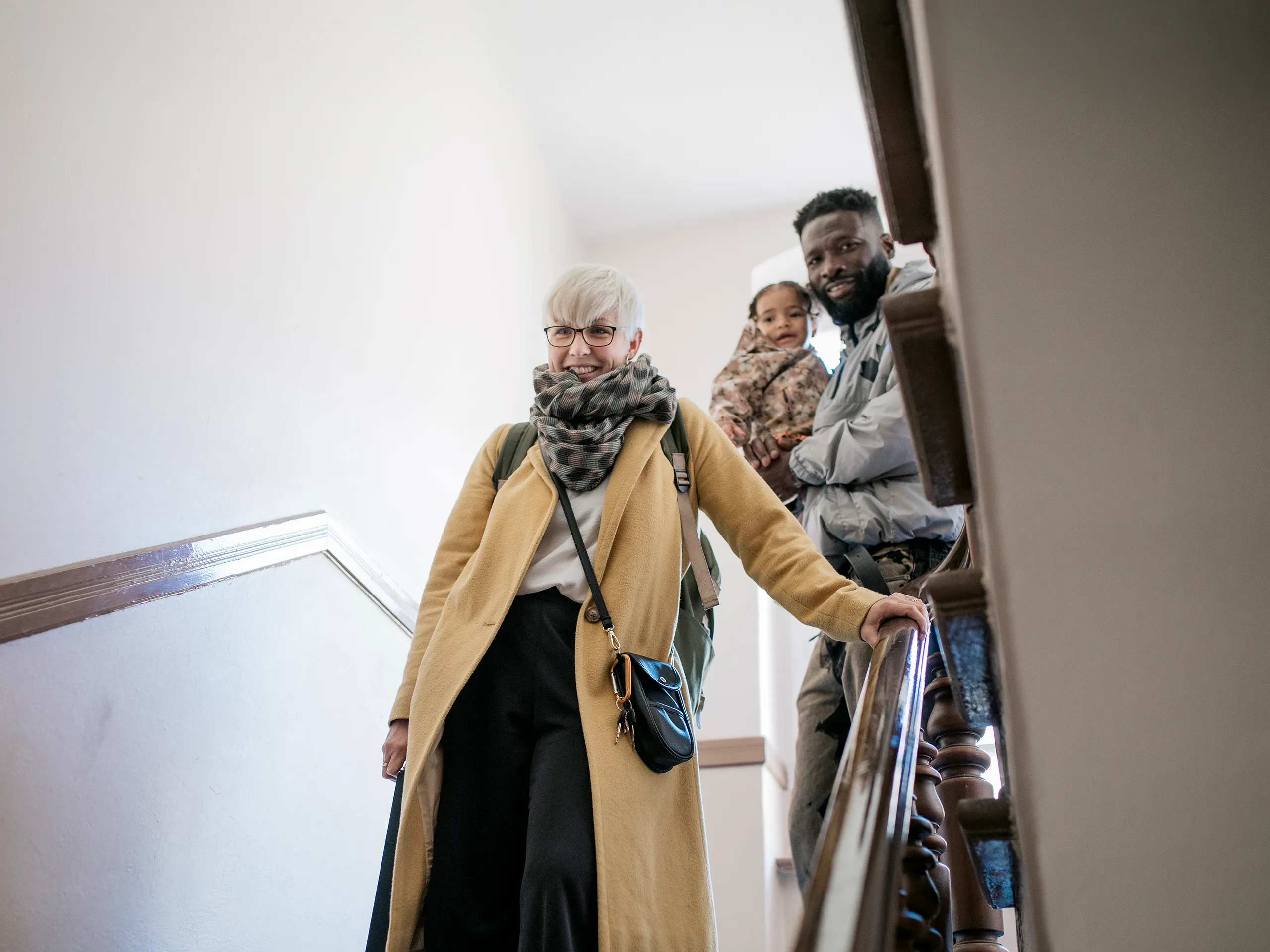 Woman with backpack walking down stairs followed by a man with a child.